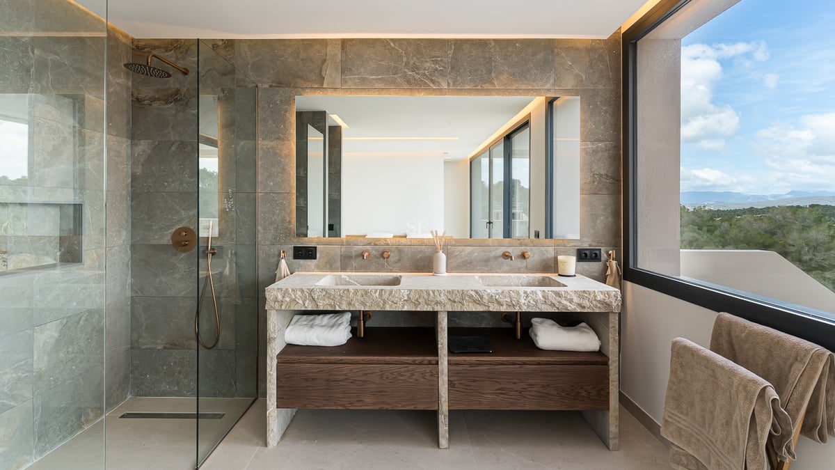 Luxuriöses Badezimmer mit Doppelwaschtisch aus Naturstein, hinterleuchtetem Spiegel und dunklen Holzakzenten.
