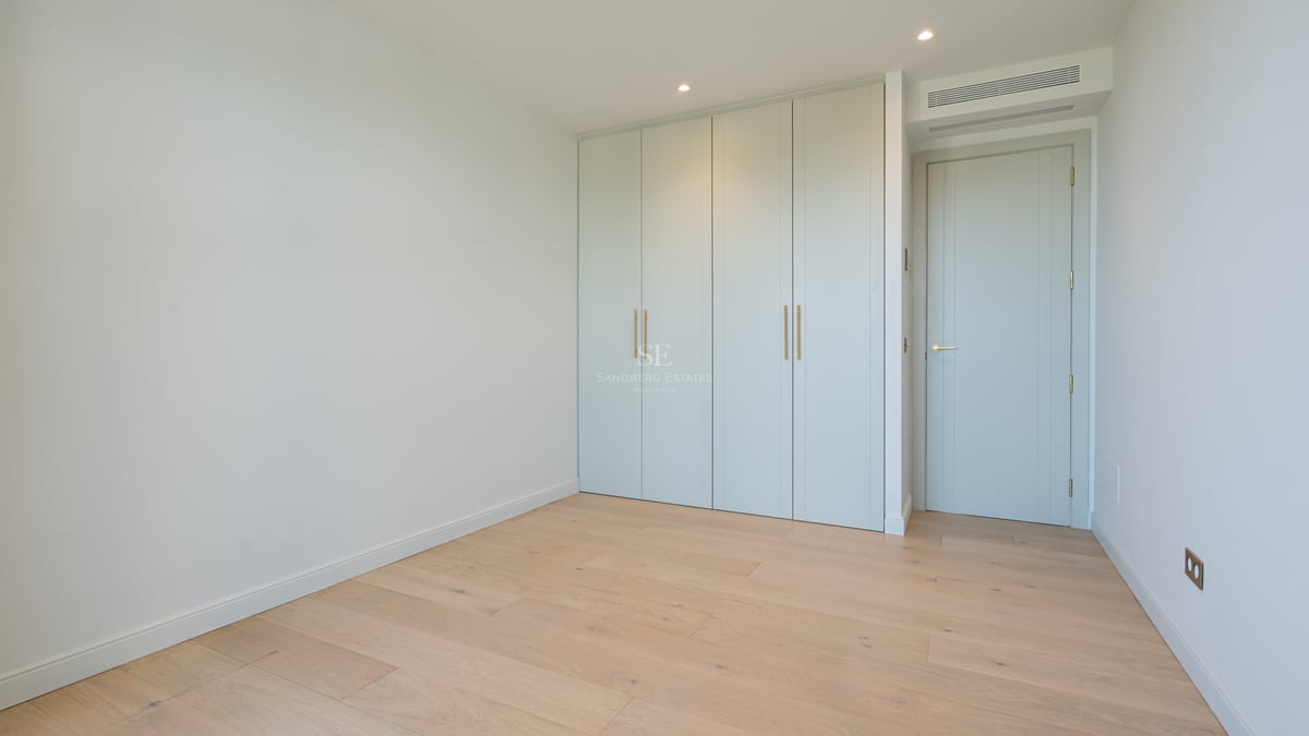 Empty room featuring light oak flooring, sage green built-in wardrobes, and minimalist white walls.