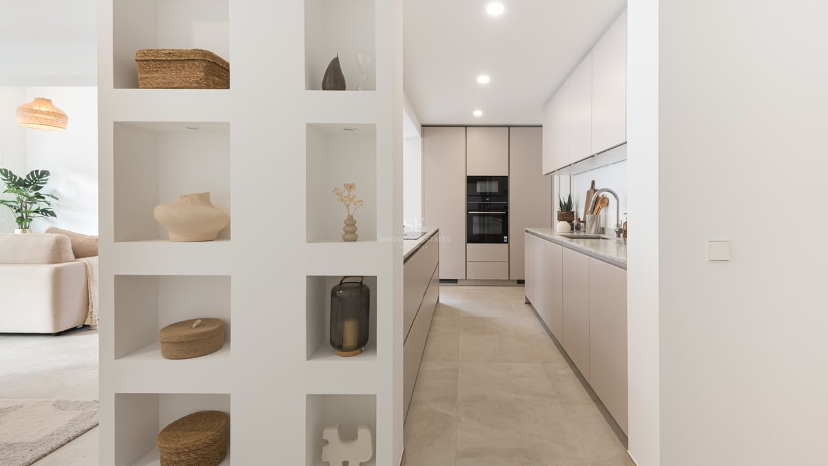 Modern galley kitchen with taupe cabinets next to a white partition wall with eight decorative recessed niches.