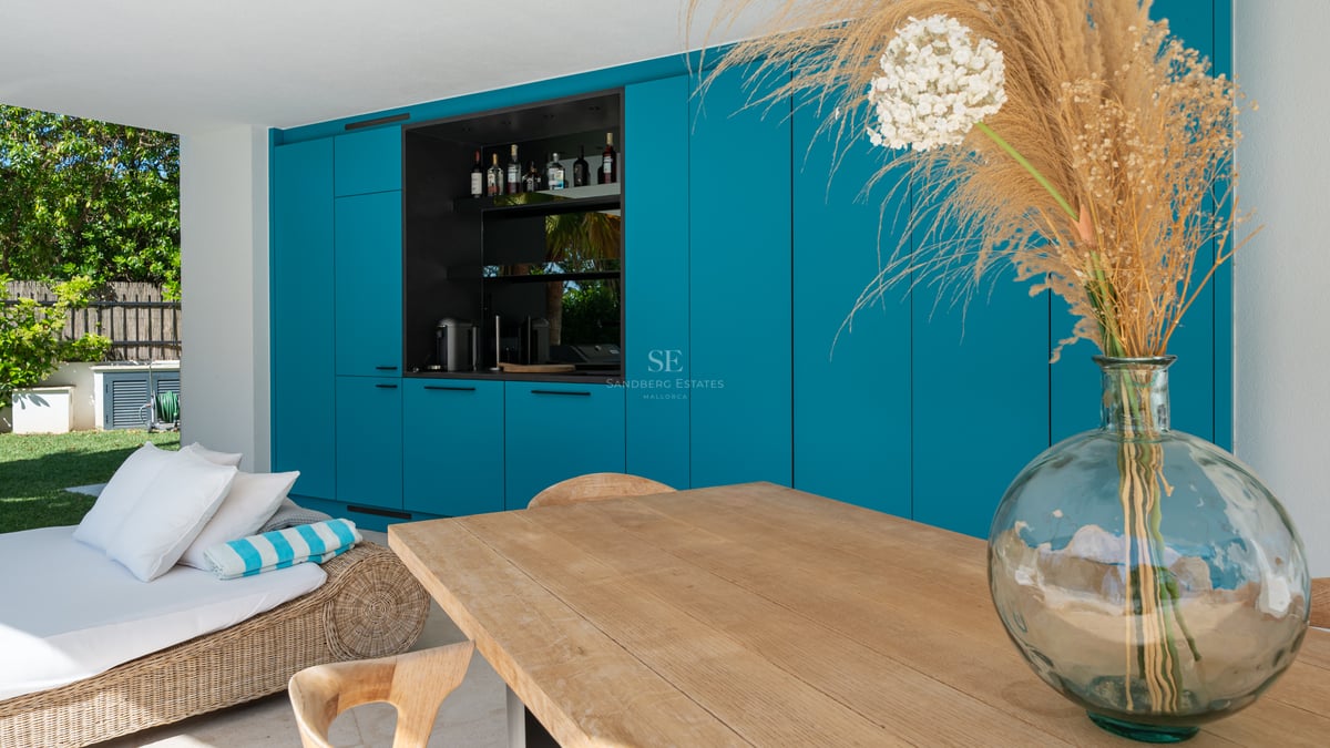 Terrasse avec armoires bleu sarcelle, station bar, table en bois clair et méridienne en osier.