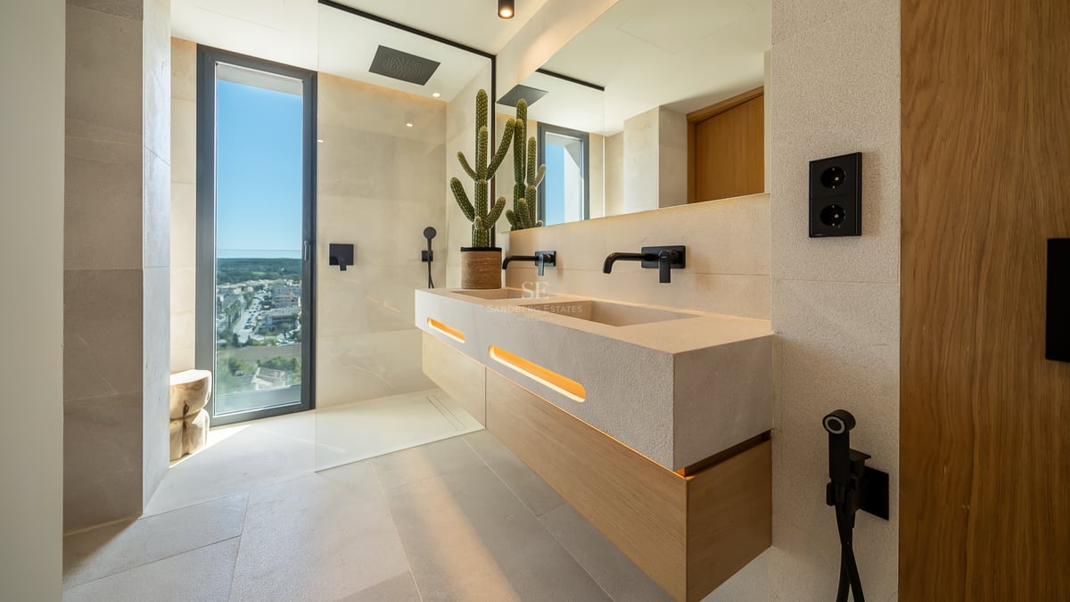 Salle de bain de luxe avec double vasque en pierre naturelle, robinetterie noir mat et grande baie vitrée.