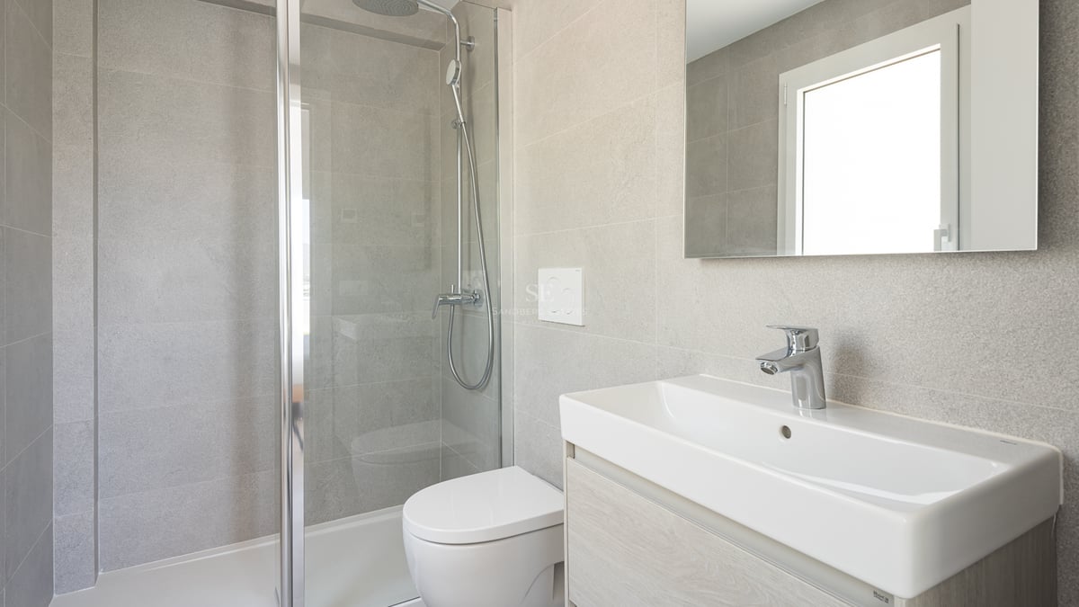 Salle de bain contemporaine avec carrelage effet pierre grise, douche vitrée, WC suspendu et meuble vasque blanc.