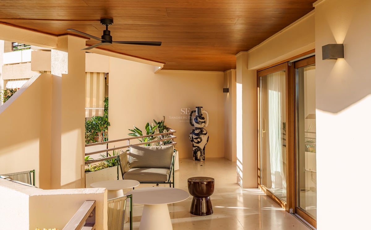 Überdachte Terrasse mit hellem Steinboden, modernen Möbeln, einem Deckenventilator und einer großen dekorativen Vase.