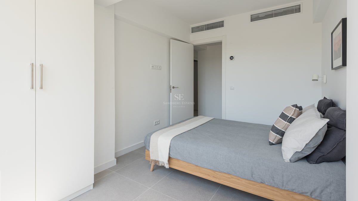 Chambre lumineuse avec cadre de lit en chêne, placards blancs et sol en grès gris dans une villa contemporaine.