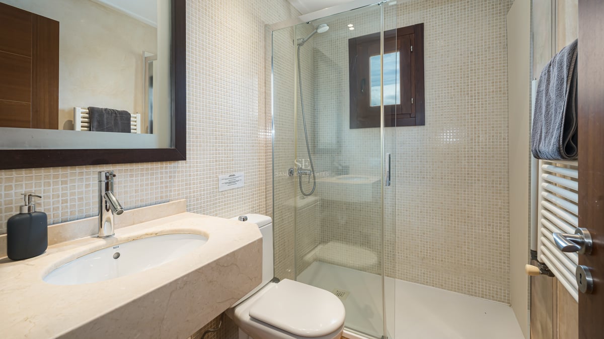 Salle de bain avec douche vitrée, murs en mosaïque beige et plan de toilette en marbre.