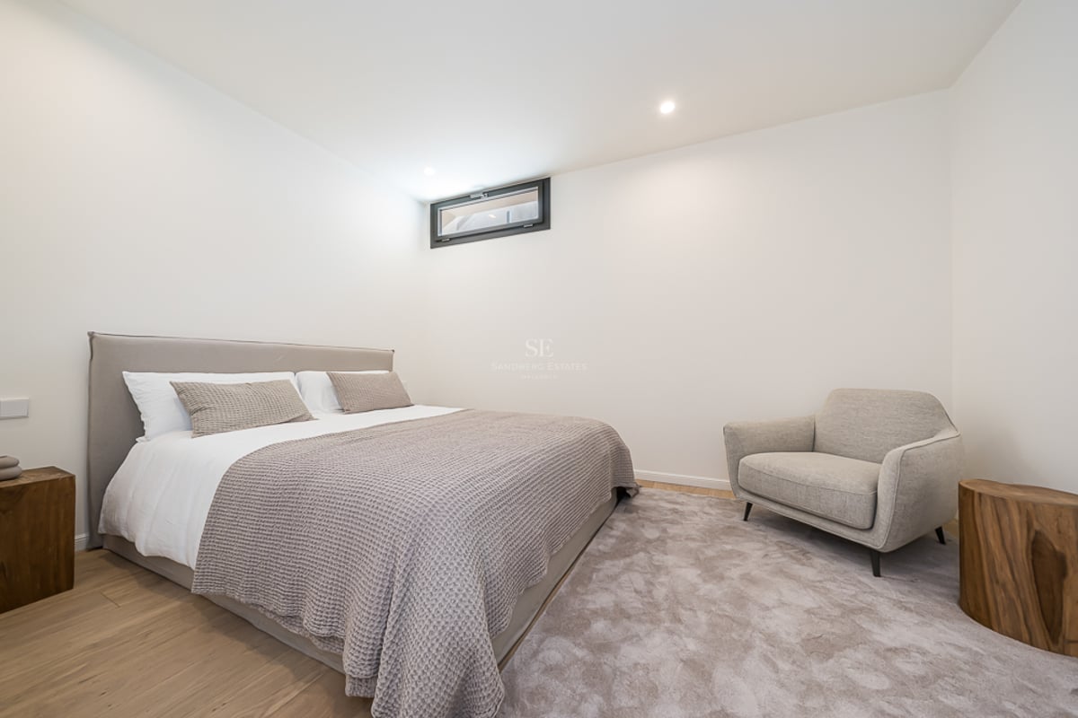 A modern bedroom with a grey upholstered bed, wooden log side tables, a grey armchair, and light oak floors.