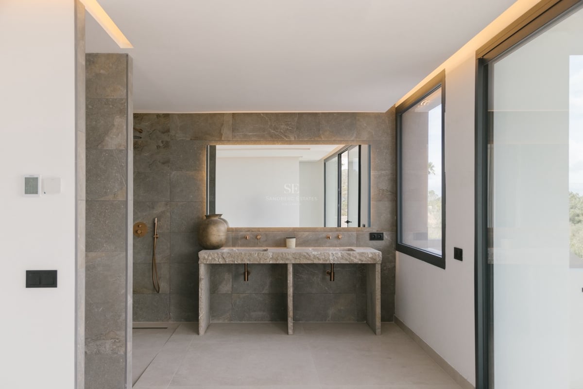 Modernes Badezimmer mit Doppelwaschtisch aus Stein, hinterleuchtetem Spiegel und Messingarmaturen.