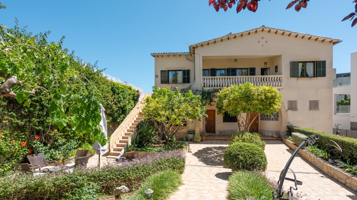 Exteriör av en medelhavsvilla i två våningar med gröna fönsterluckor, stentappa och en anlagd innergård.