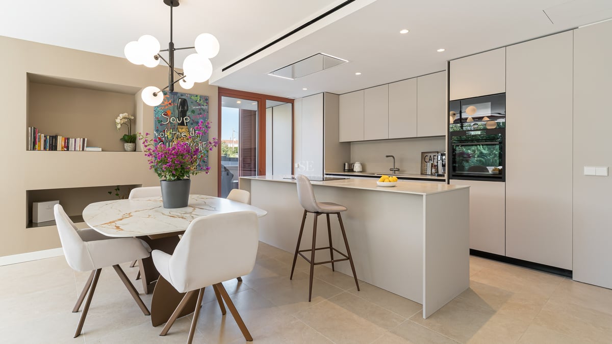Modern kitchen featuring a cream island, marble dining table with white chairs, and contemporary pendant lighting.