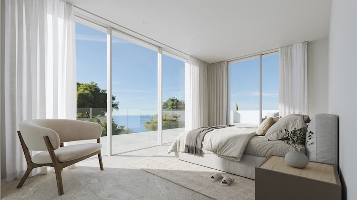 Chambre principale minimaliste dotée de baies vitrées du sol au plafond s'ouvrant sur une terrasse en pierre avec vue mer.