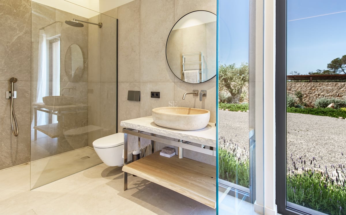 Zeitgenössisches Badezimmer mit Naturstein-Aufsatzwaschbecken, Rundspiegel und ebenerdiger Dusche.