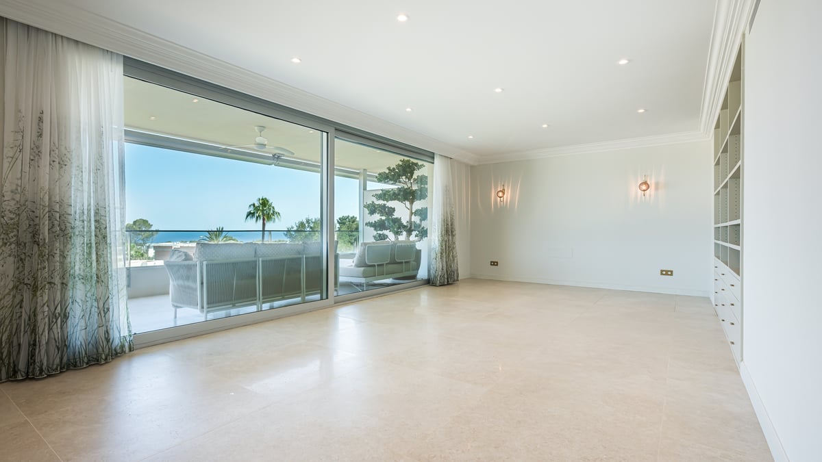 An empty luxury living room with marble floors and large glass doors opening to a terrace with sea views.
