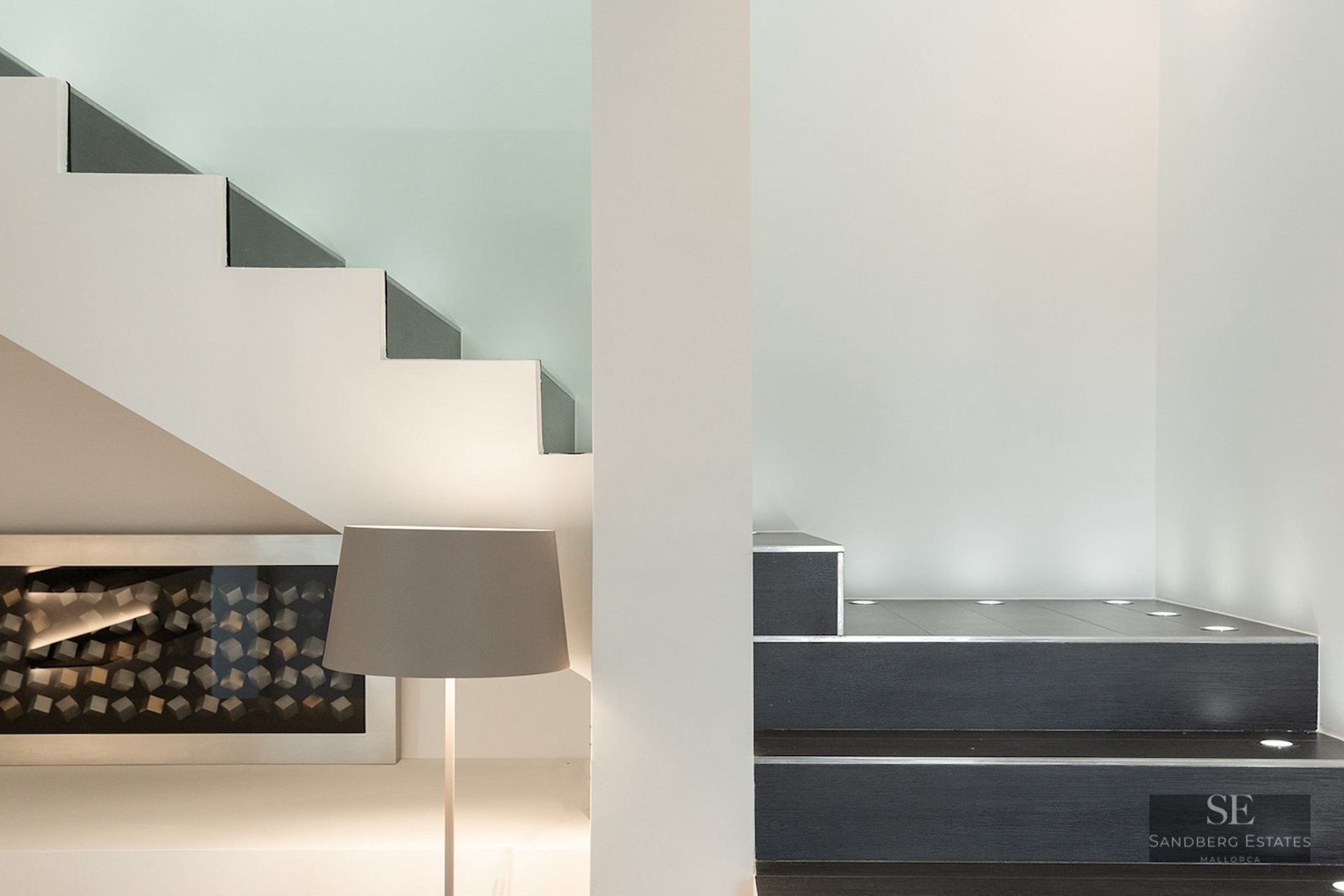 Close-up of a minimalist staircase with dark steps, white walls, and circular recessed floor lights.