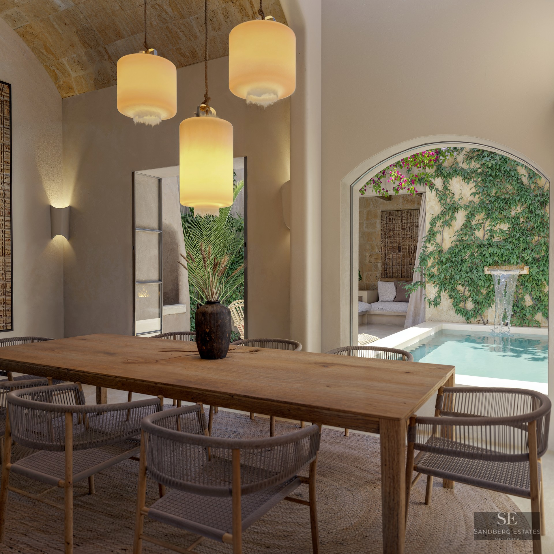 A large wooden dining table with woven chairs under three pendant lights, looking out to a courtyard plunge pool.