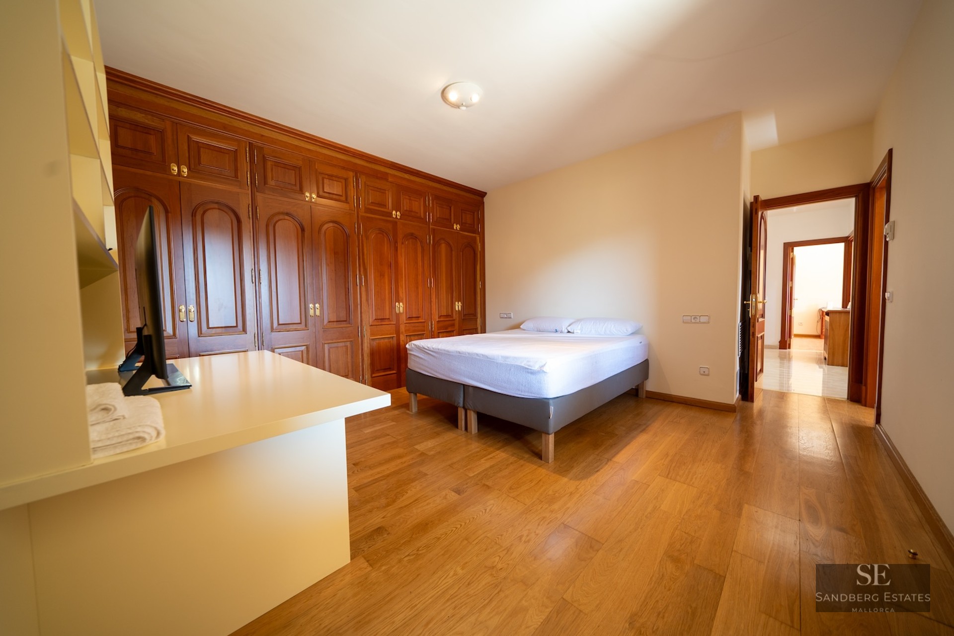 Bright bedroom featuring large built-in wooden closets, hardwood floors, and a minimalist double bed.