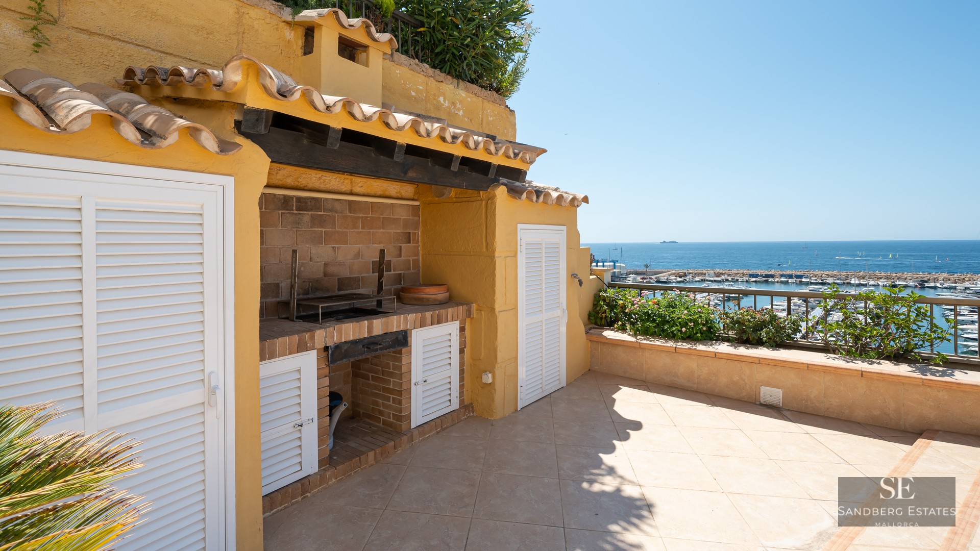 Outdoor terrace featuring a brick BBQ area, yellow stucco walls, and a view of a marina and the blue ocean.