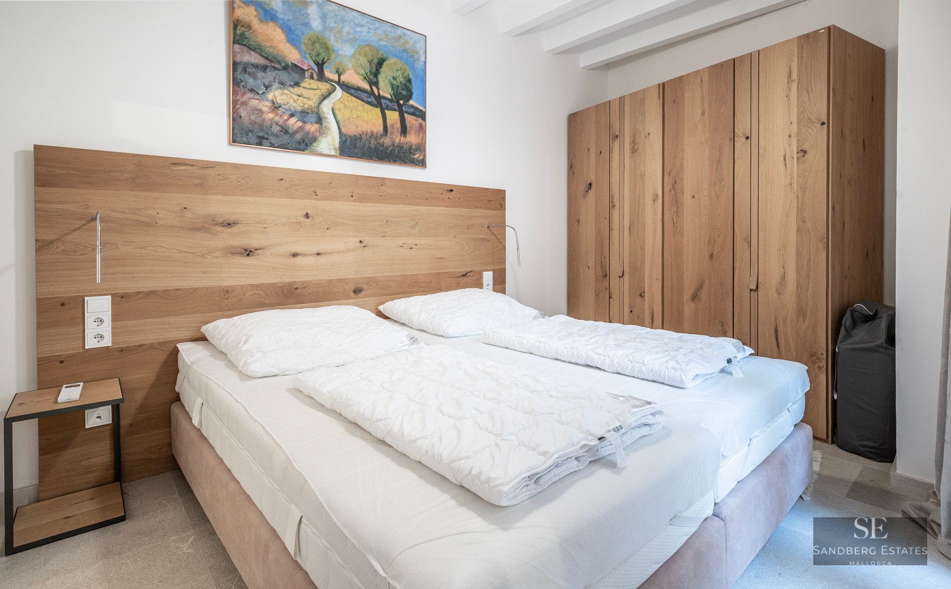 Modern bedroom with a large oak wardrobe, wooden headboard, and a double bed with crisp white linens.