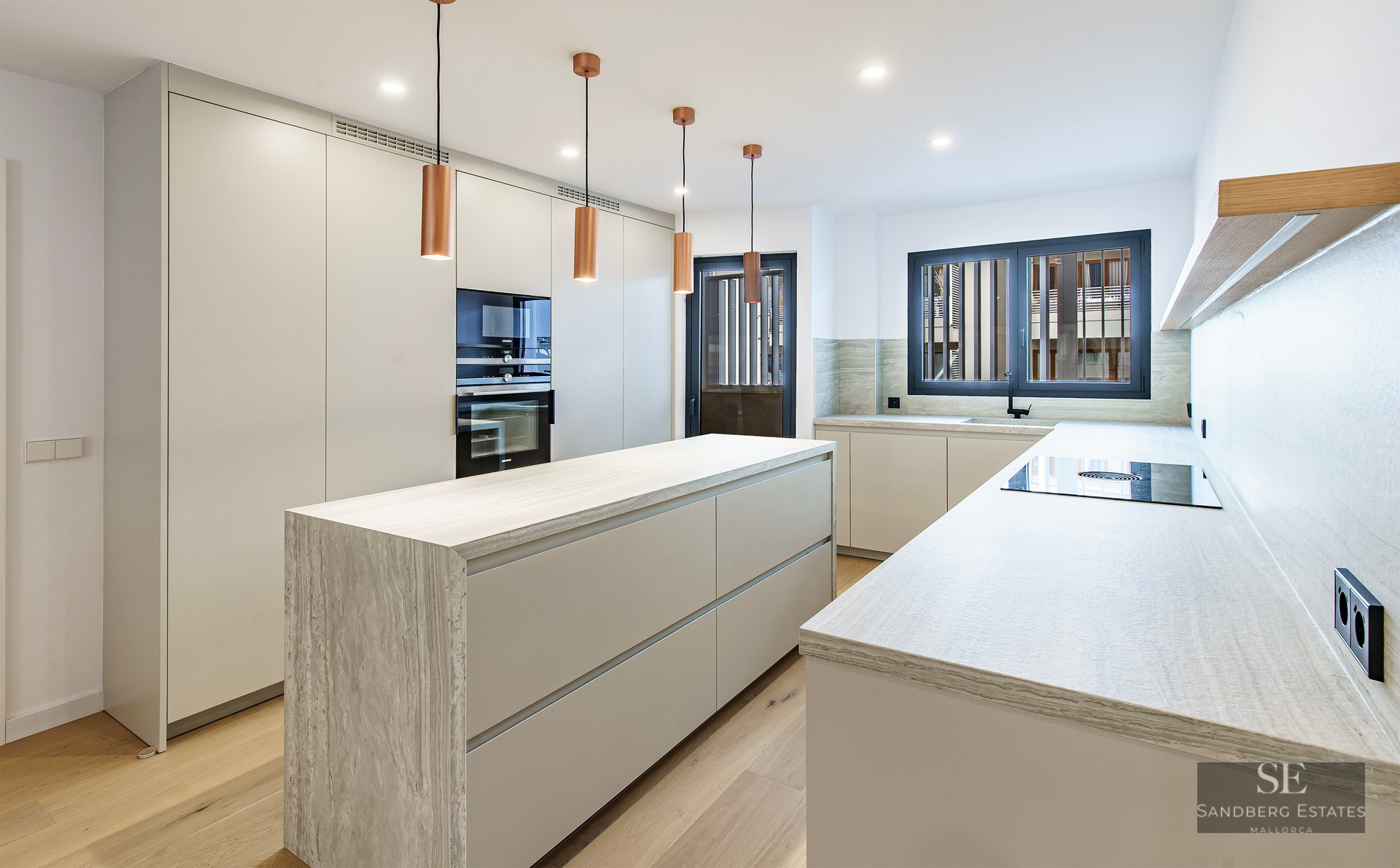 Cuisine contemporaine blanche avec îlot en pierre, suspensions en cuivre et parquet en bois.