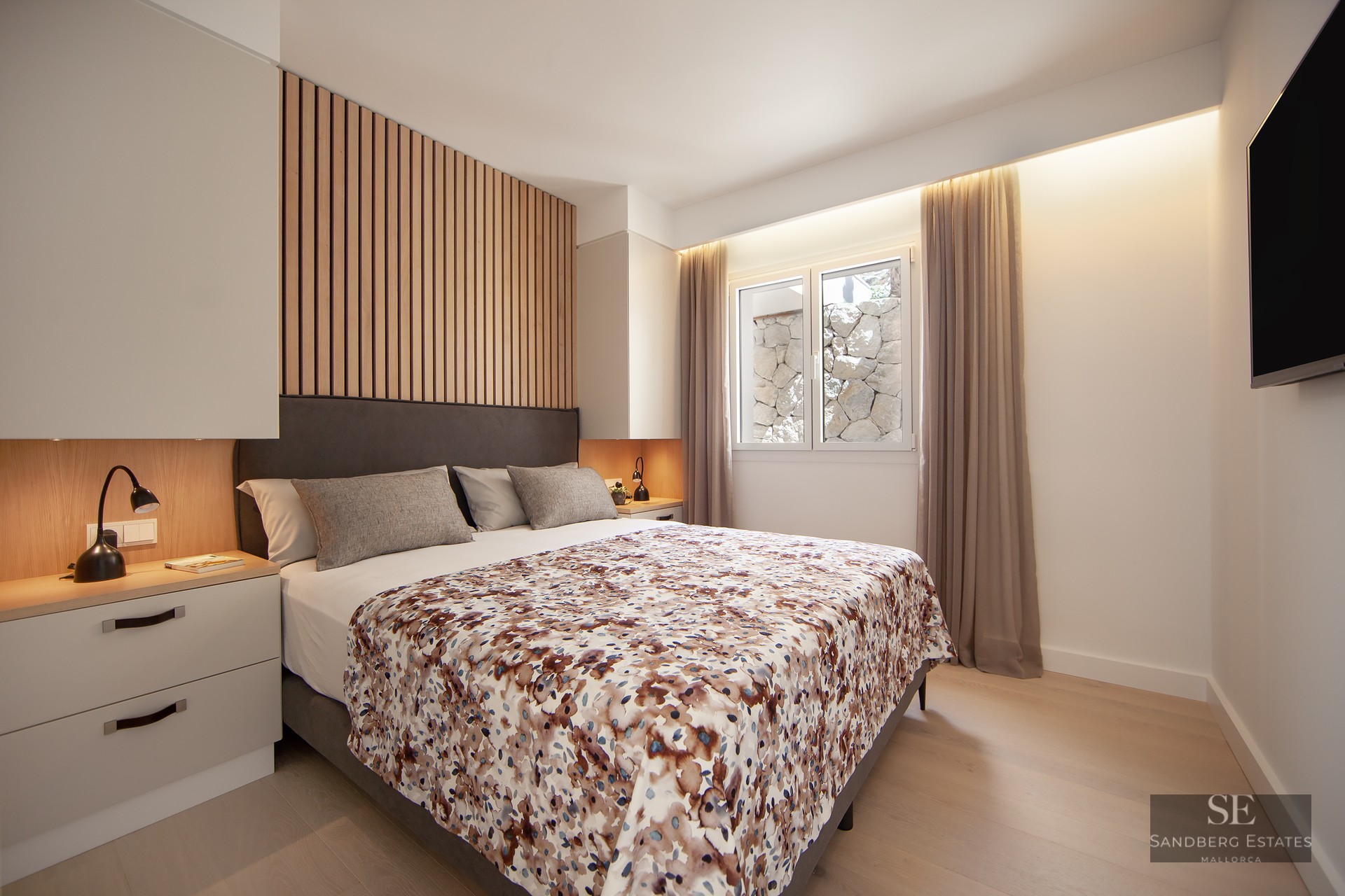 Modern master bedroom featuring a grey bed, wood slat headboard detail, warm bedside lighting, and a window.
