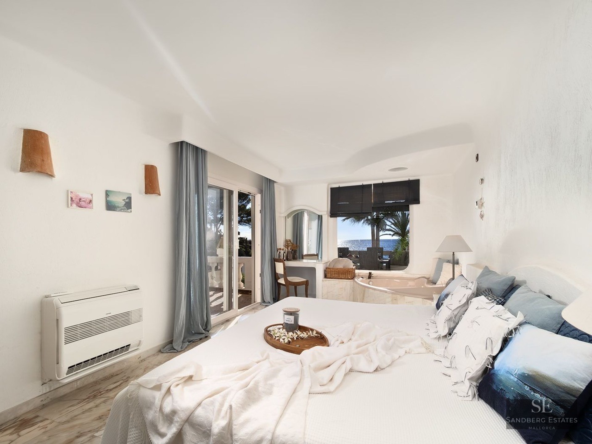 Bright white master bedroom featuring a built-in bathtub by the window and a balcony overlooking the sea.