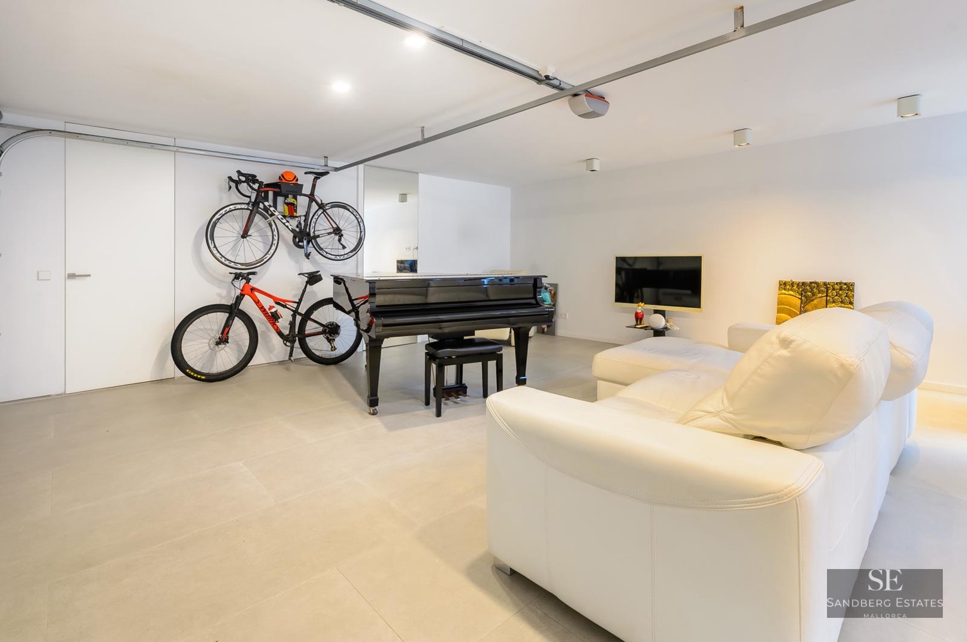 Modern white room featuring a black grand piano, wall-mounted bicycles, and a white leather sofa on grey tiled floors.