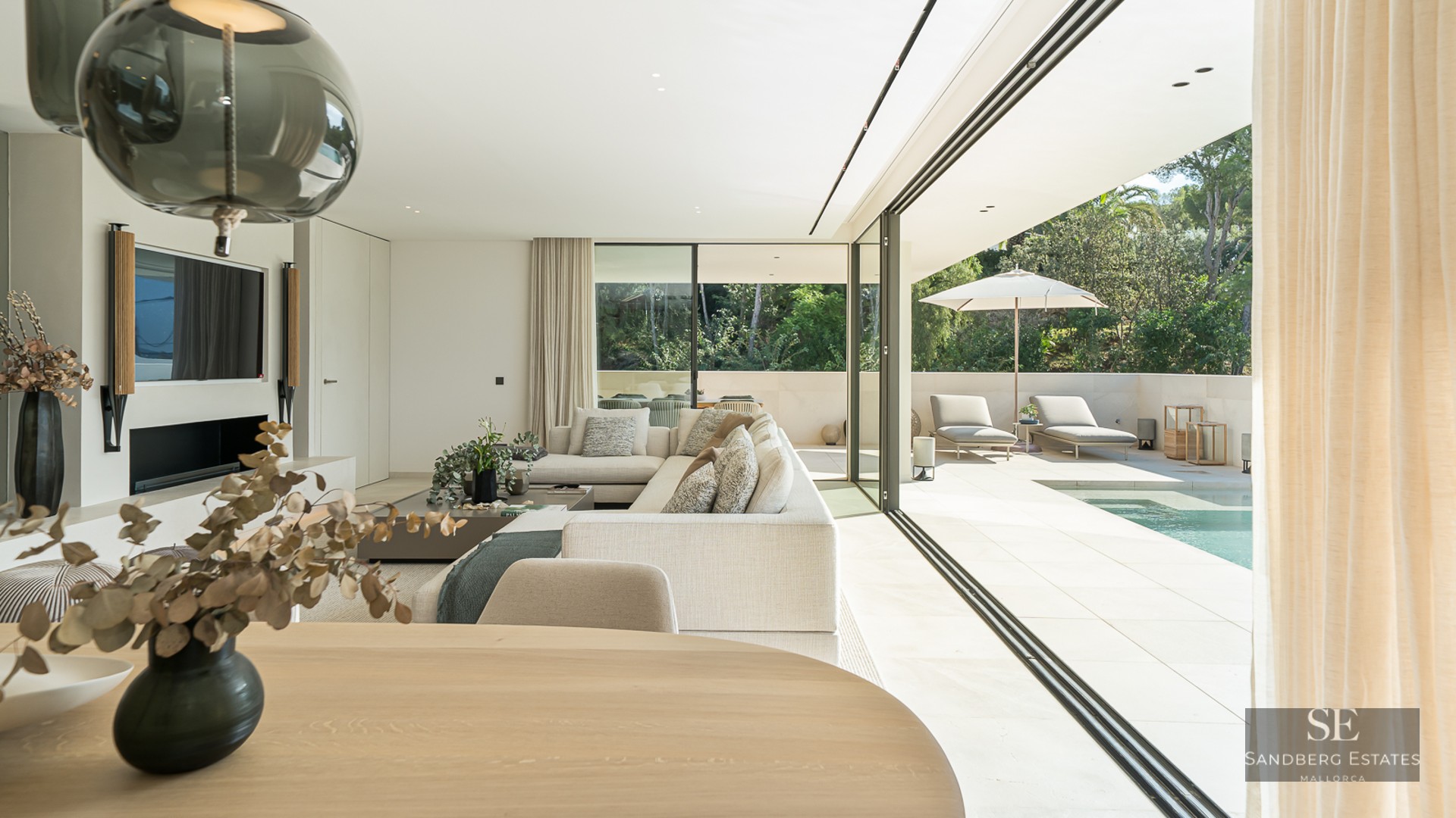 Modern bright living room with large glass doors opening to a sunlit terrace and private swimming pool.