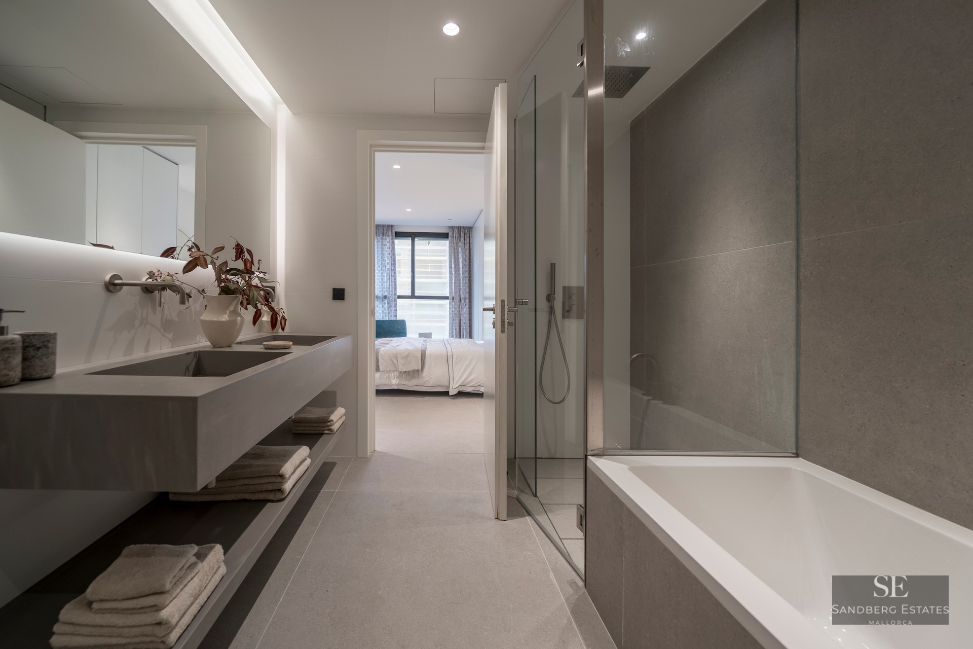 Contemporary bathroom featuring a gray floating double sink, glass shower, bathtub, and a view into the bedroom.
