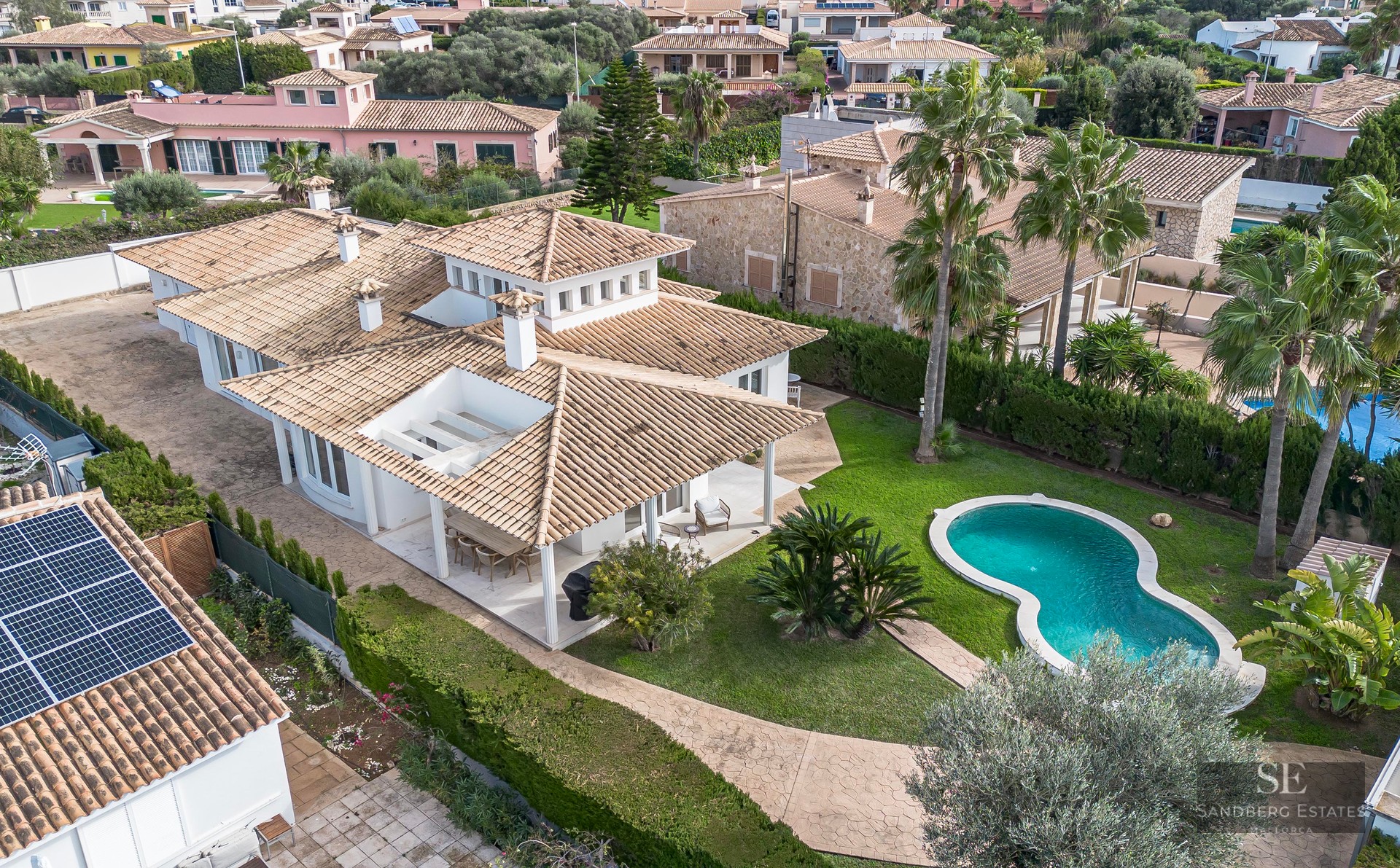 Aerial view of a white villa with a terracotta roof, a turquoise swimming pool, and a lush green garden.