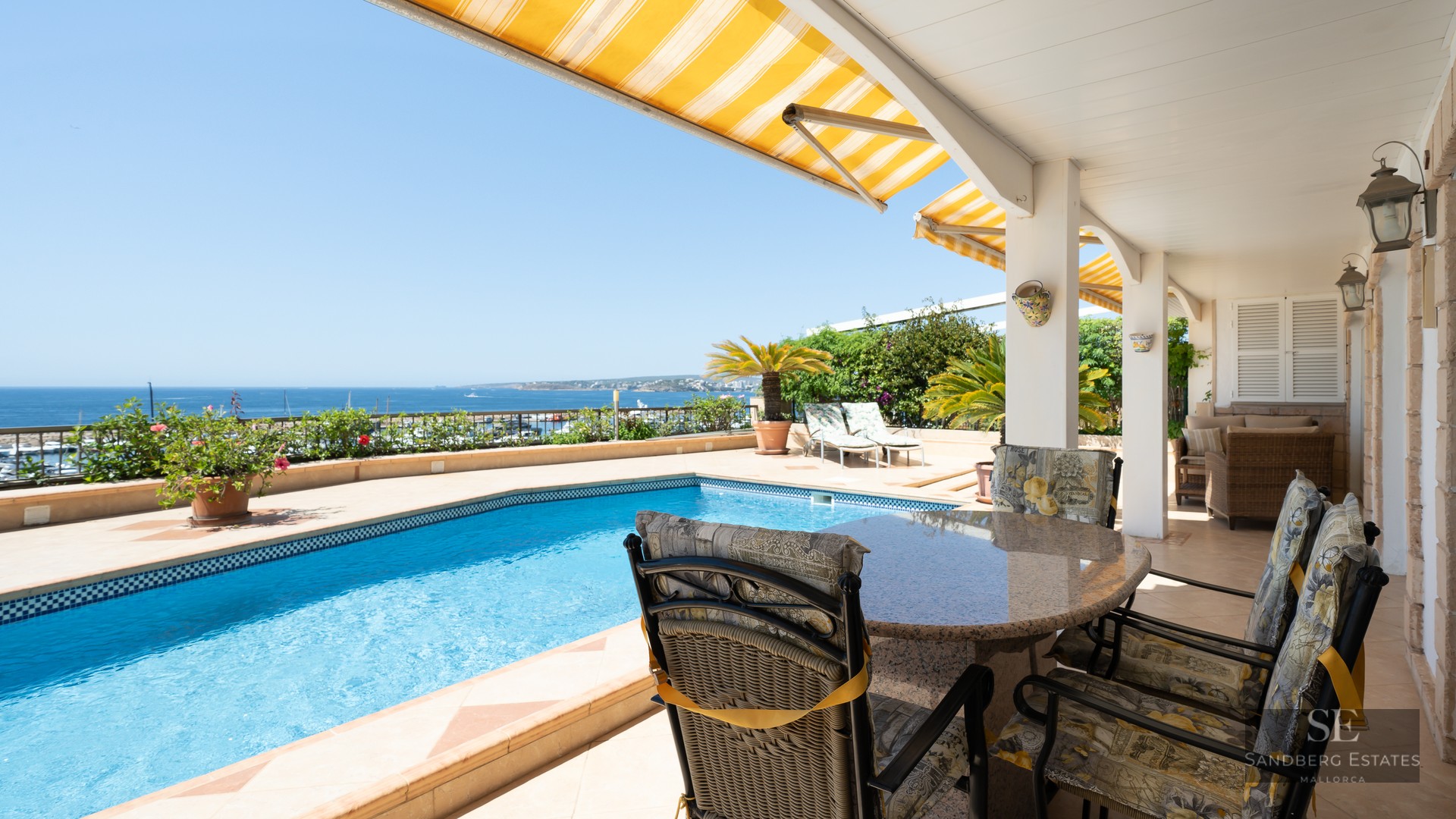 Outdoor terrace featuring a blue swimming pool, dining set, and yellow awnings with panoramic ocean views.