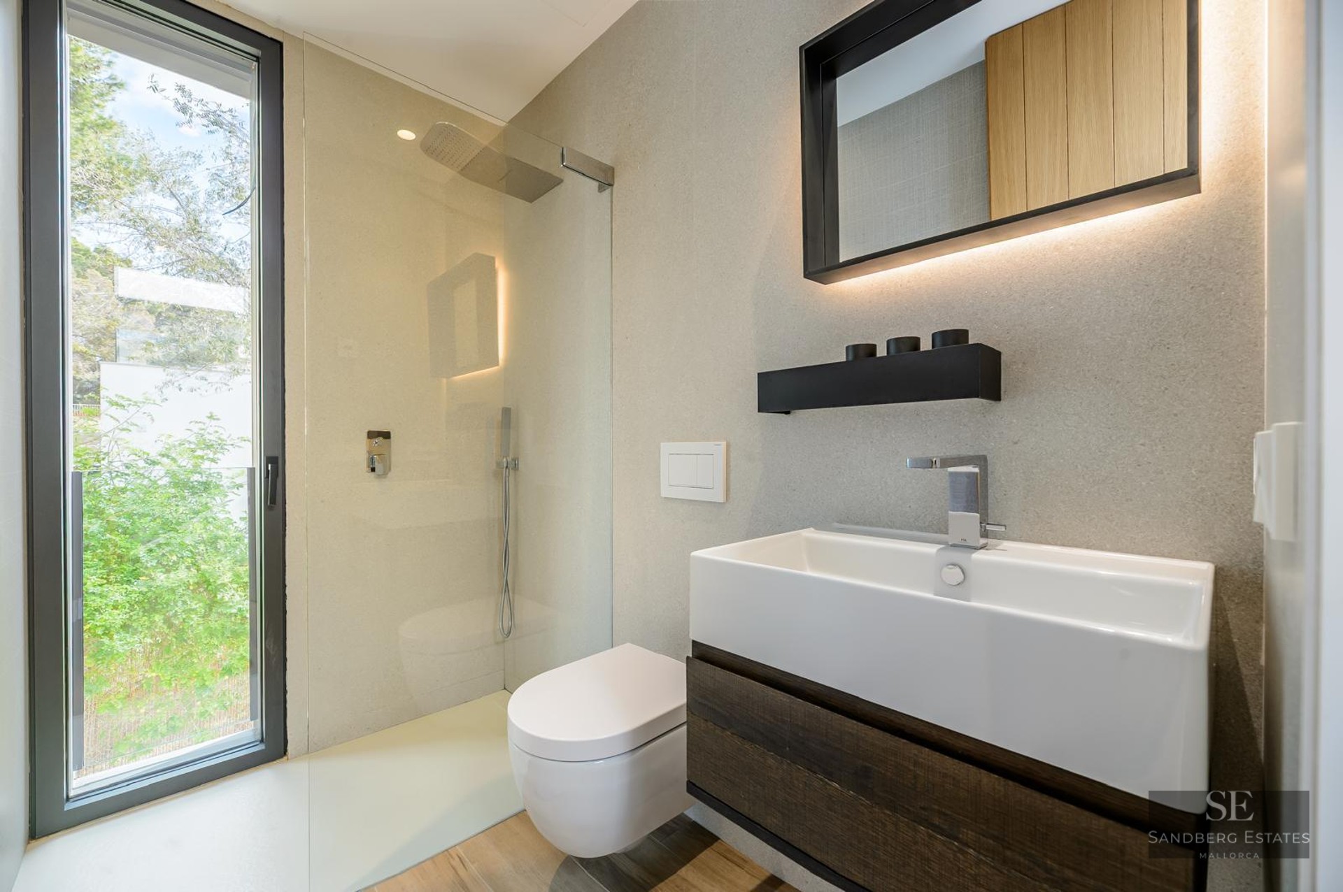 Modern bathroom featuring a white vessel sink, dark wood vanity, walk-in glass shower, and large window with green views.