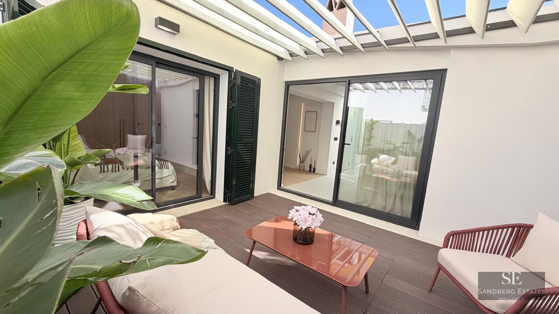 Outdoor patio with white pergola, wooden deck, terracotta-colored furniture, and tropical plants.