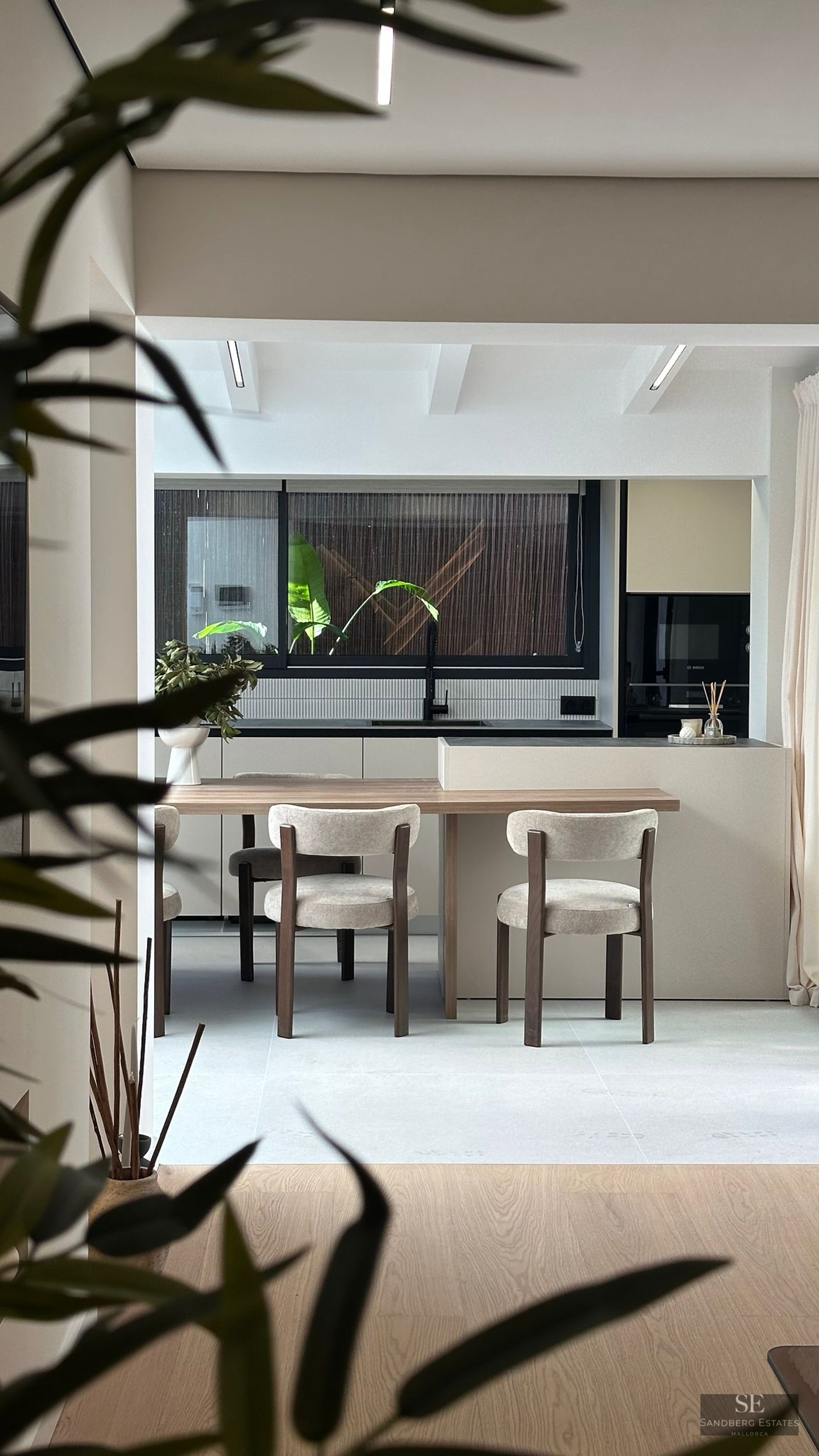 Modern kitchen featuring a light wood dining table attached to a beige island, with stylish chairs and a large window.