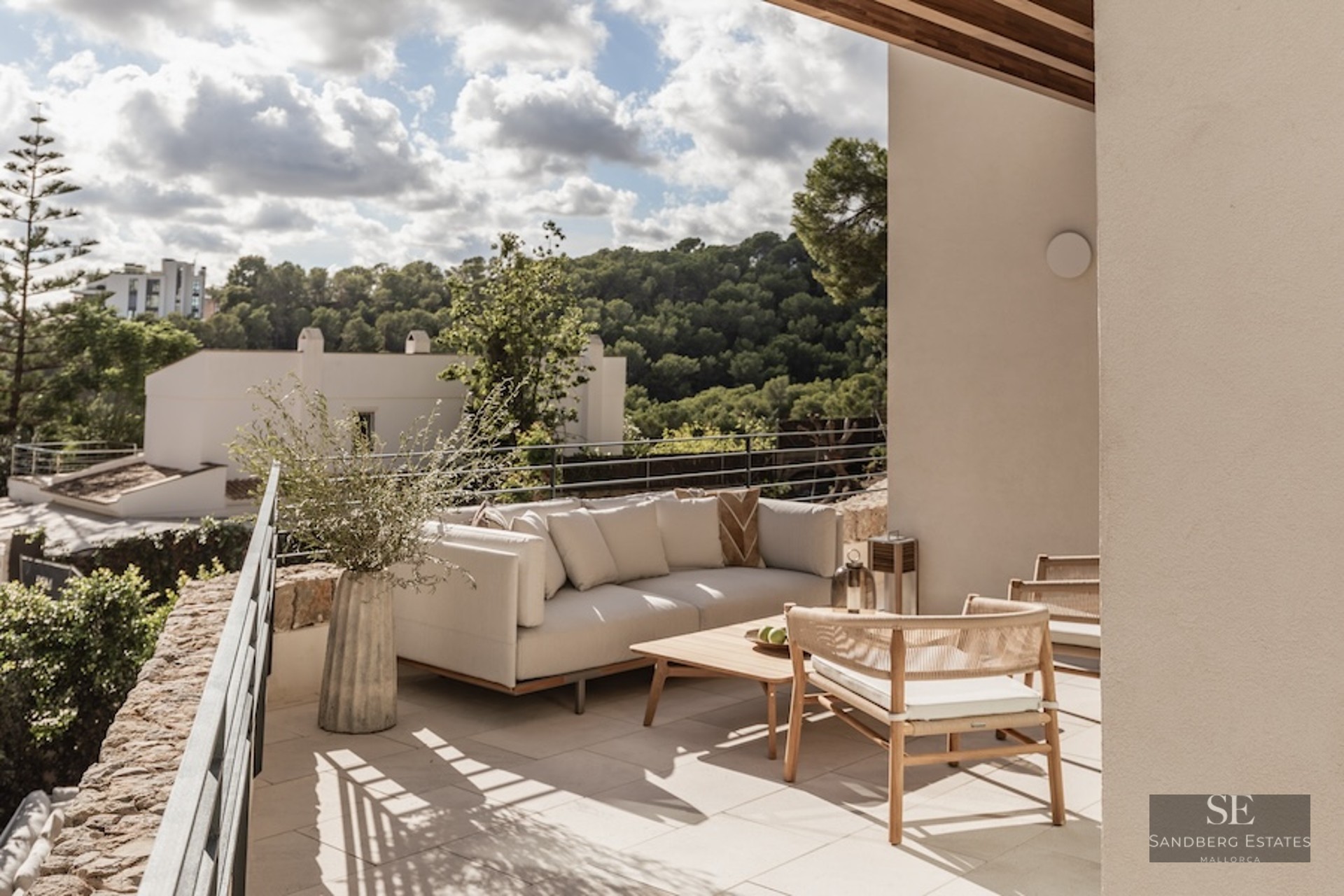 Outdoor terrace with modern sofa, wooden table, and woven chairs overlooking a lush green valley.
