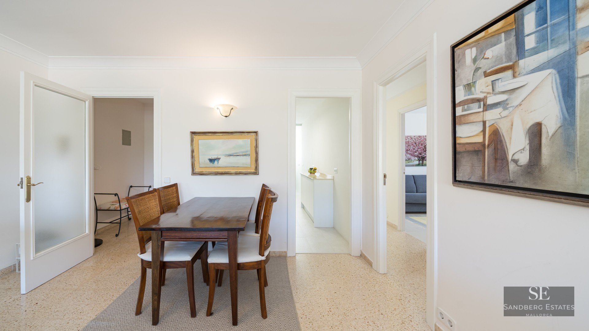 A dark wood dining table and four chairs with woven backs and white cushions in a bright, white room.