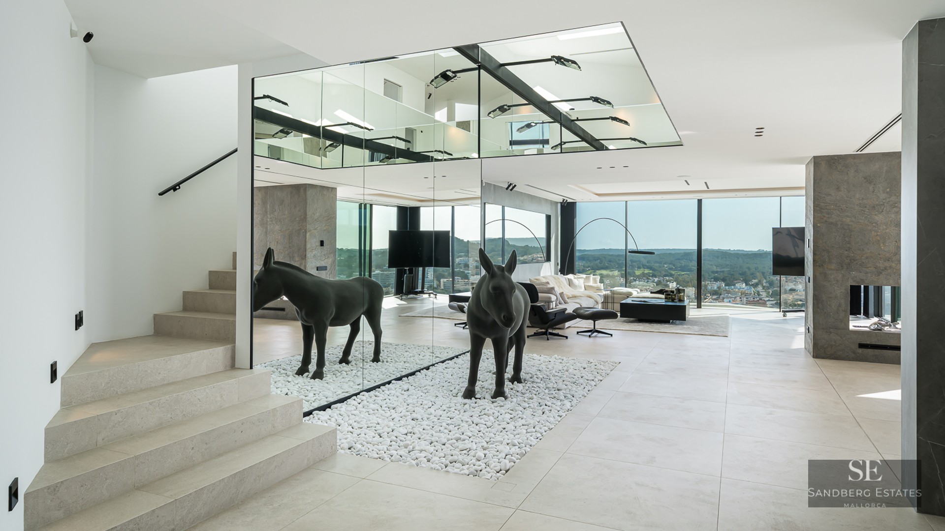 Modern living room featuring a mirrored wall, black donkey sculpture on white pebbles, stone stairs and views.