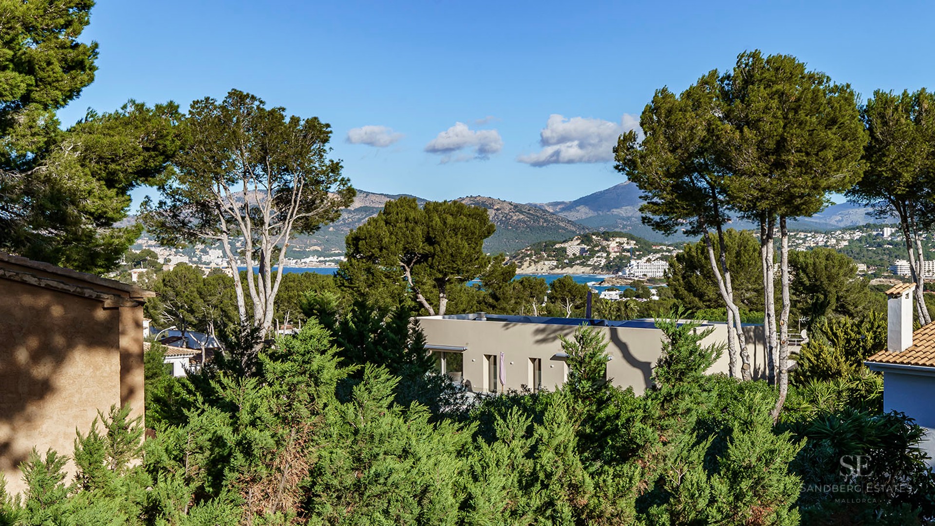 Modern villa nestled in pine trees with Mediterranean sea and mountain views in the distance.
