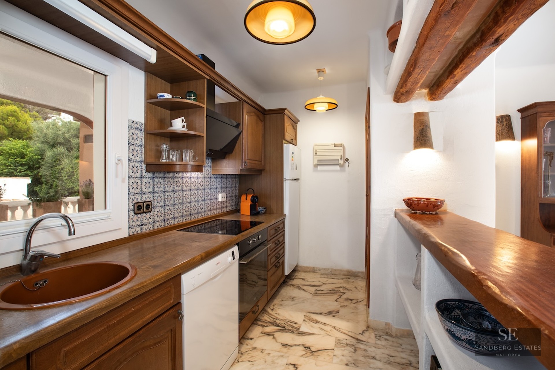 Narrow kitchen featuring dark wood cabinets, marble flooring, exposed beams, and traditional patterned tiling.