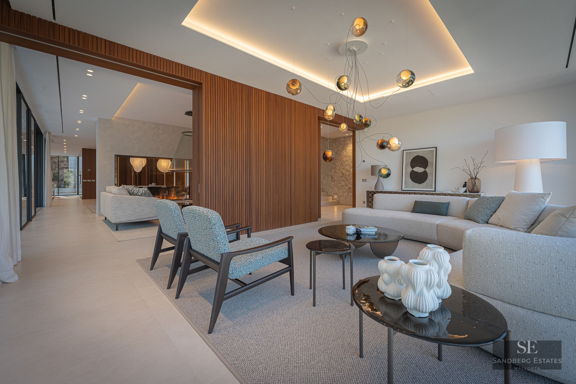 Modern living room with a large gray sofa, blue armchairs, wood slatted wall, and a unique glass orb chandelier.