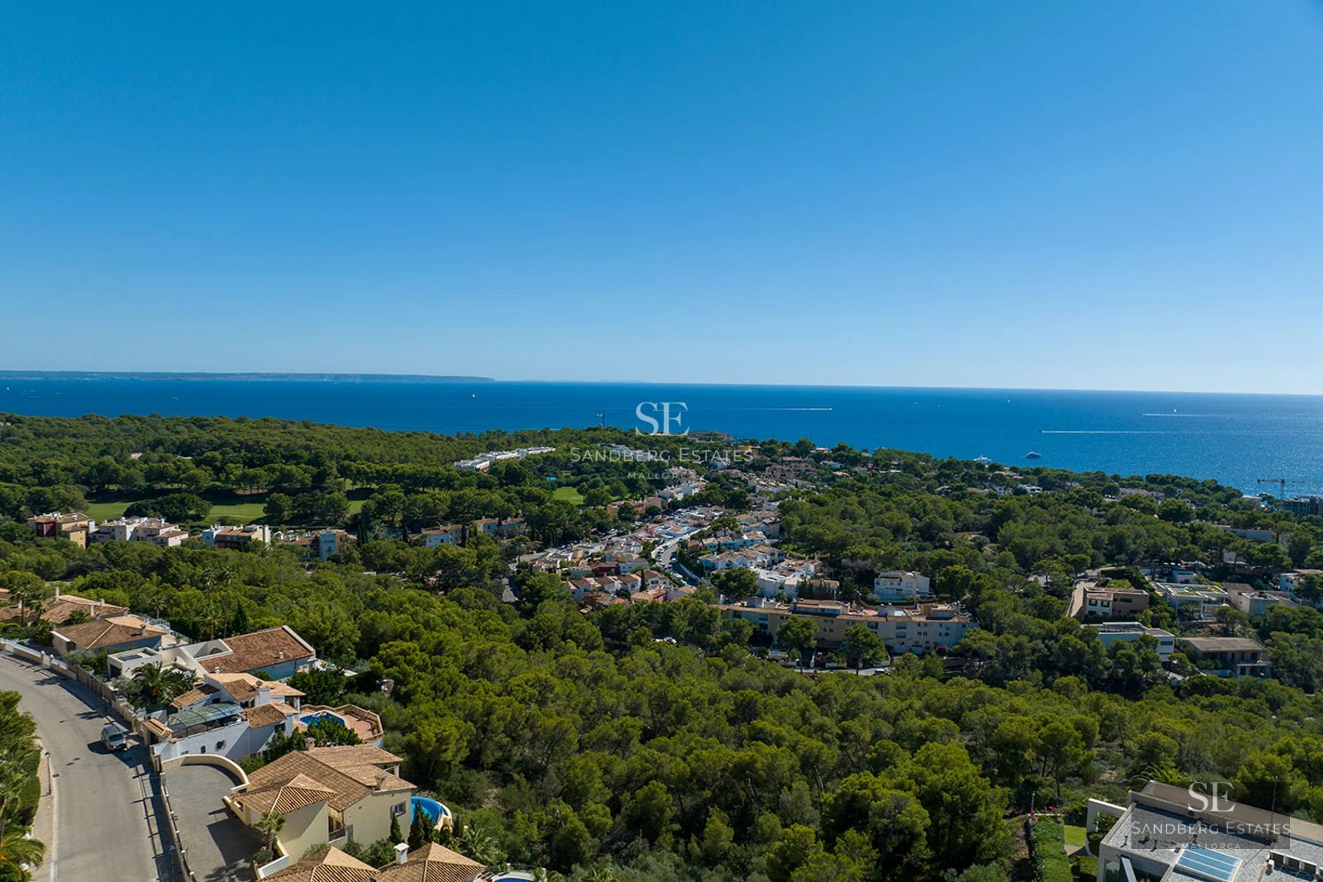 Aerial view of a Mediterranean coastal town with lush pine forests, terracotta roof houses, and the deep blue sea.