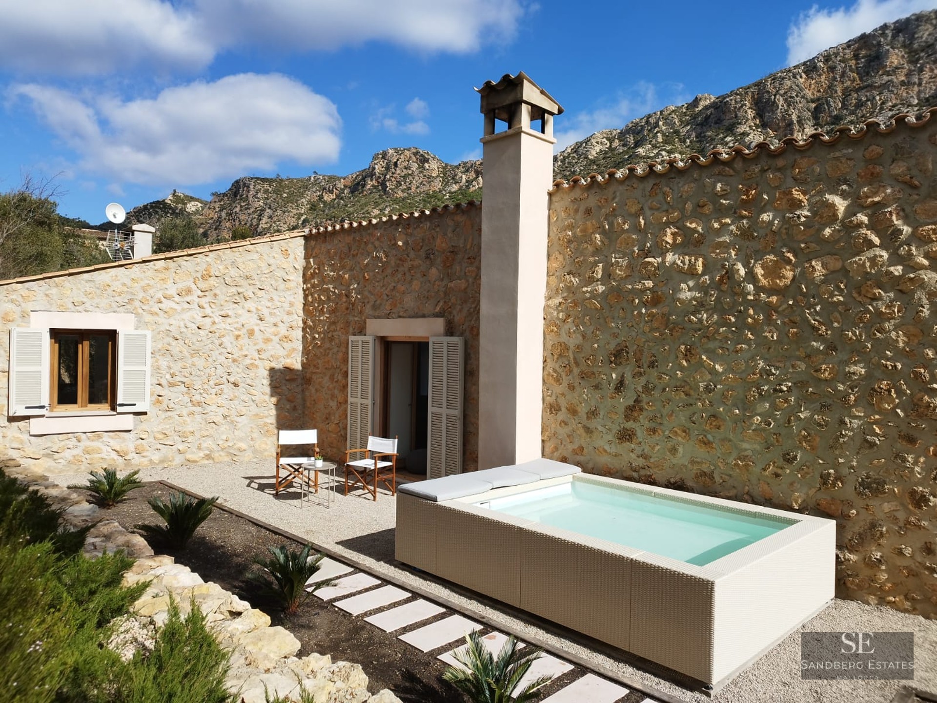 Small rectangular plunge pool on a gravel terrace next to a stone house with mountain views.
