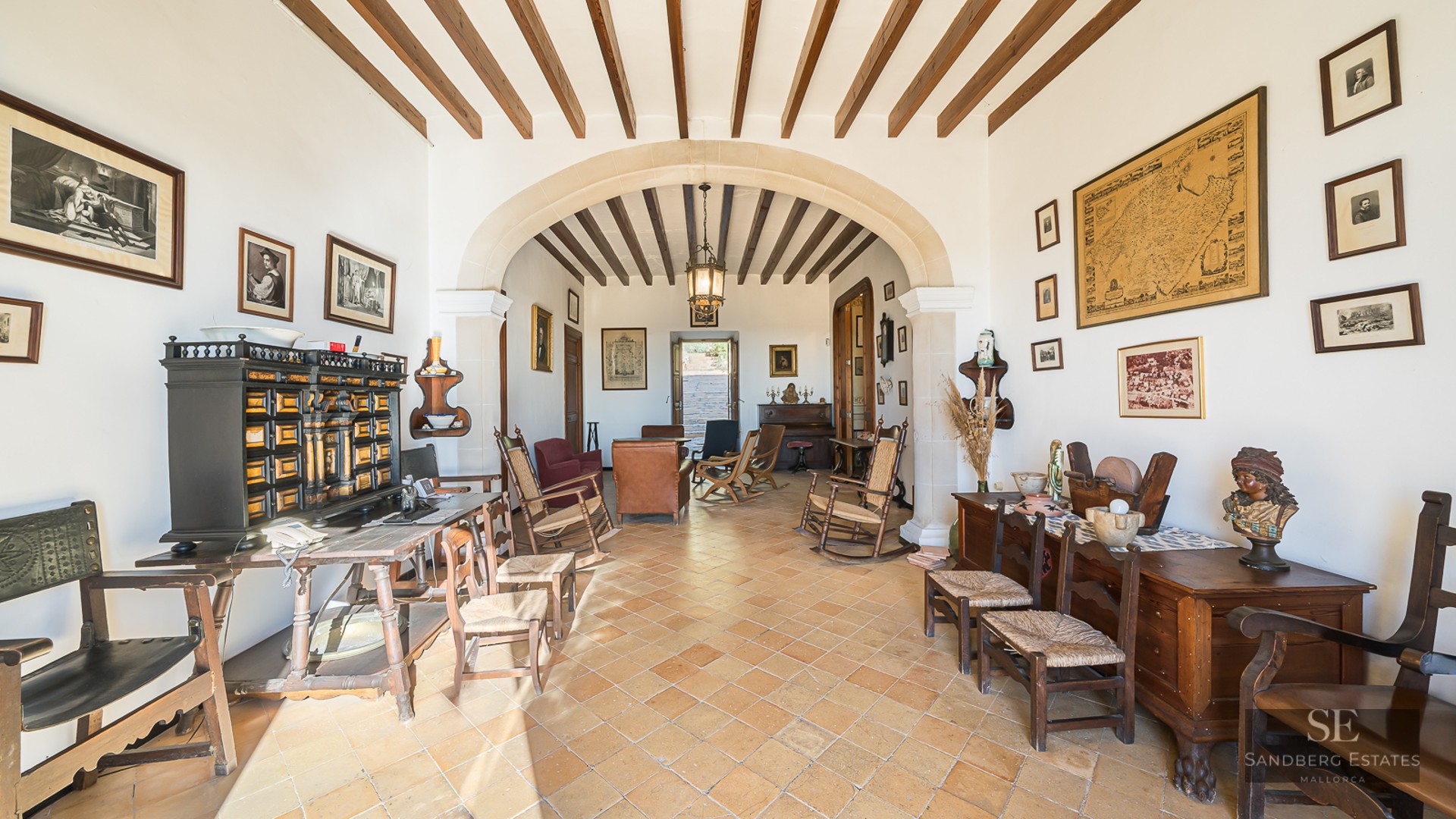 Spacious living room with terracotta floors, exposed wooden beams, a large stone archway, and rustic antique furniture.