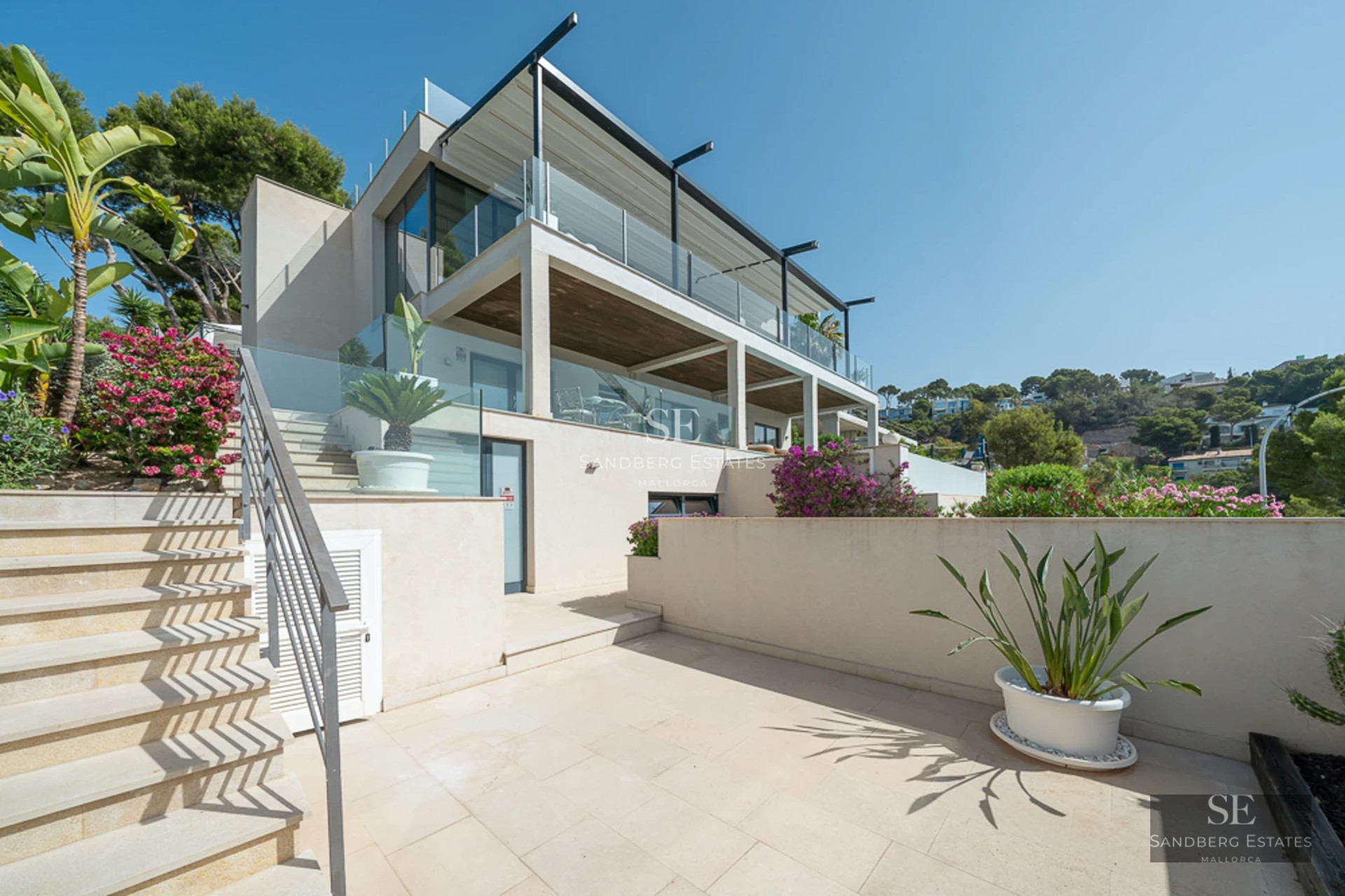 Exterior view of a modern villa featuring a swimming pool, manicured garden, and spacious terraces. Minimalist design with large windows.