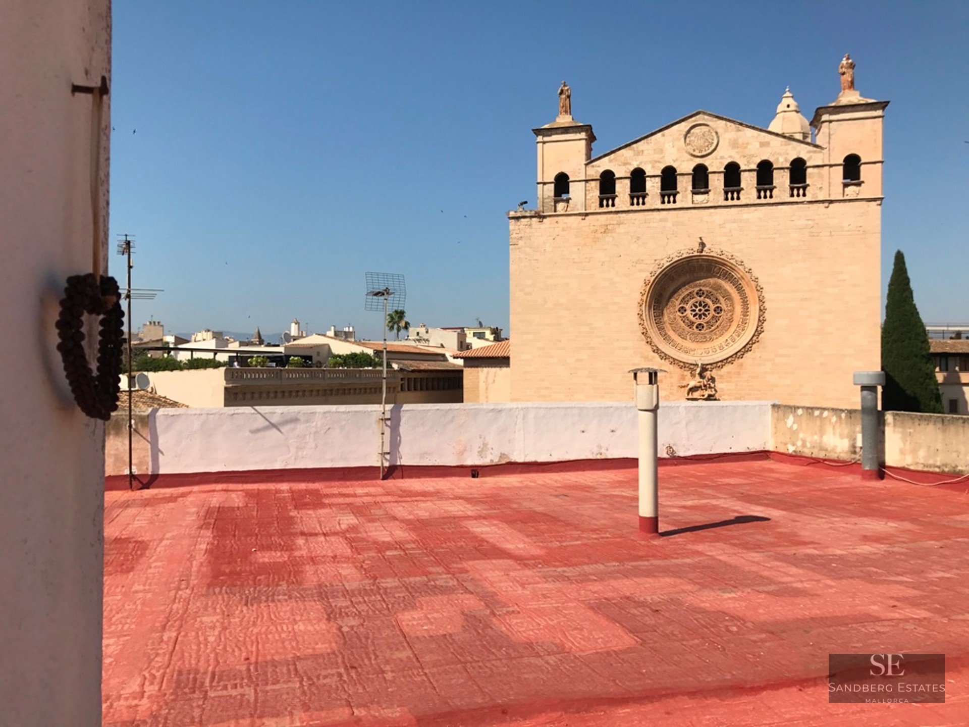 Red tiled rooftop overlooking a stone church facade with a rose window under a clear blue sky.
