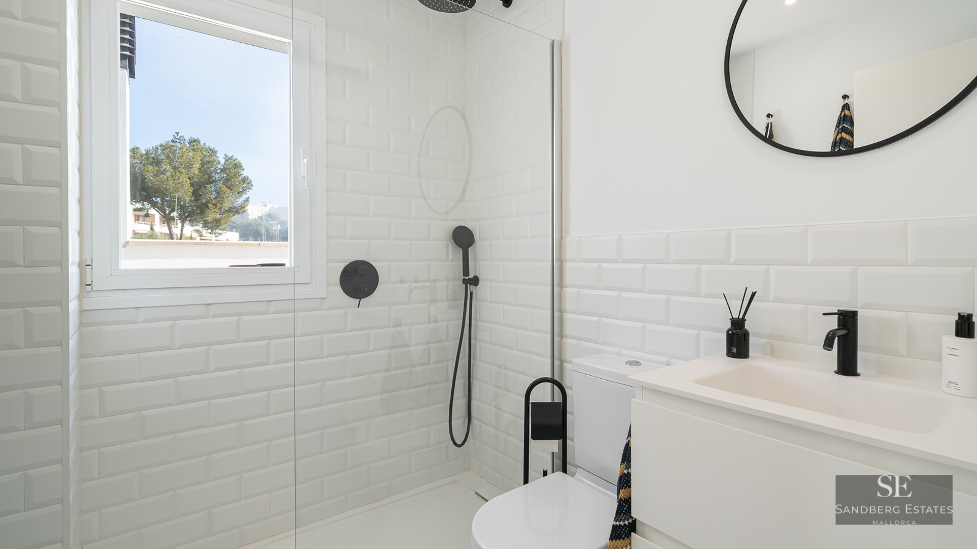 Bright bathroom featuring white subway tiles, a glass shower partition, and modern matte black fixtures.