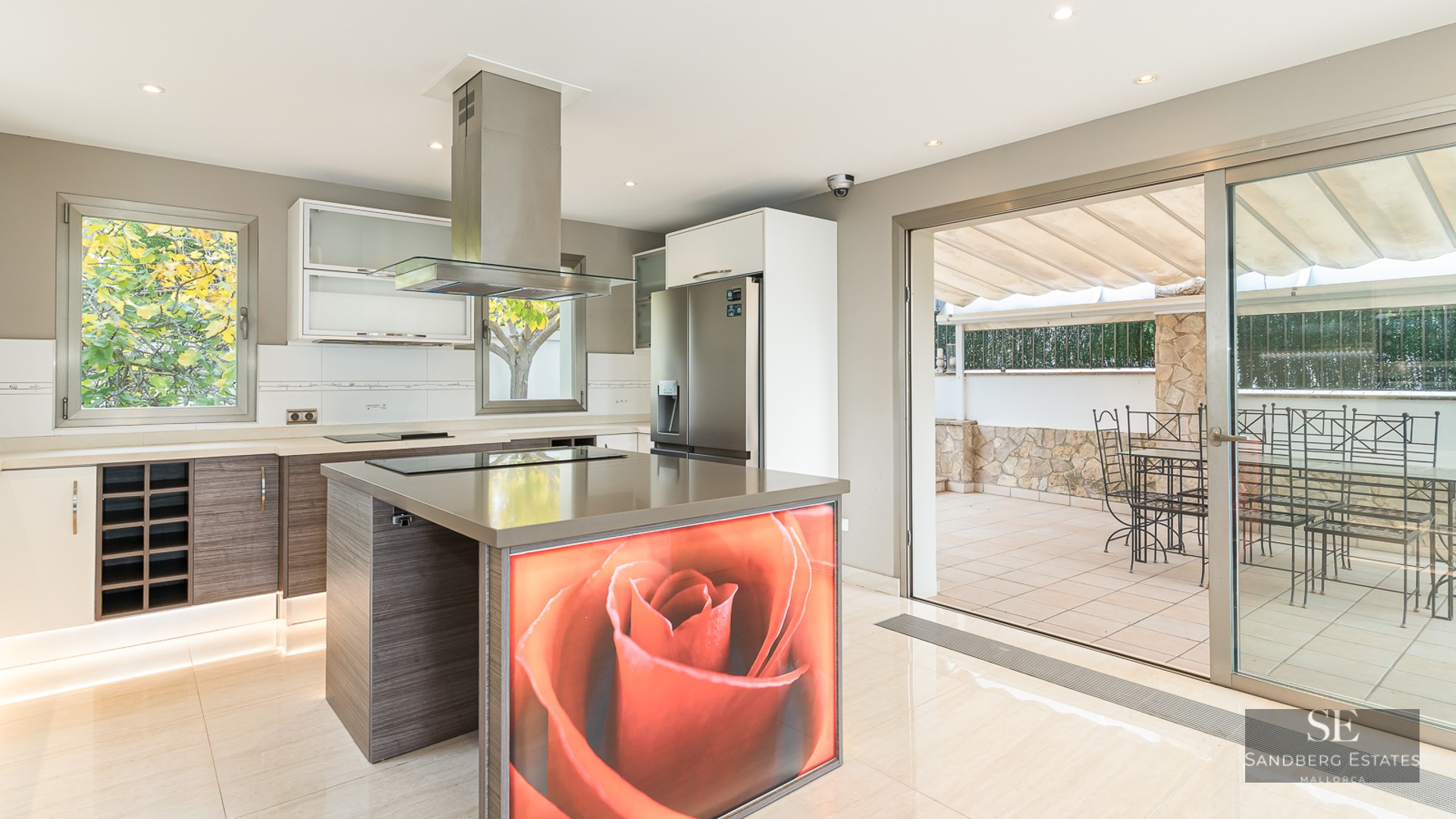 Modern kitchen featuring a large island with a red rose graphic, stainless steel appliances, and patio doors.