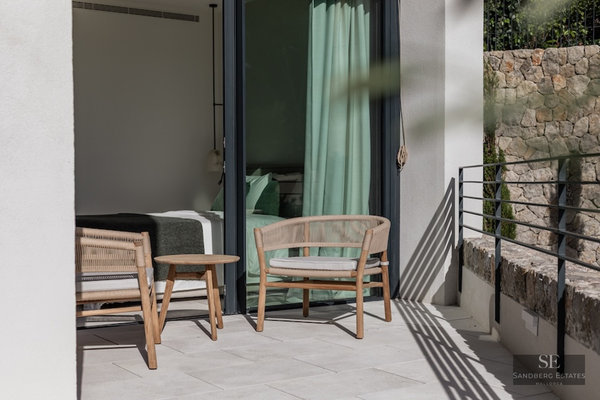 Modern terrace with woven armchairs and a small wooden table, adjacent to a bedroom with large glass sliding doors.