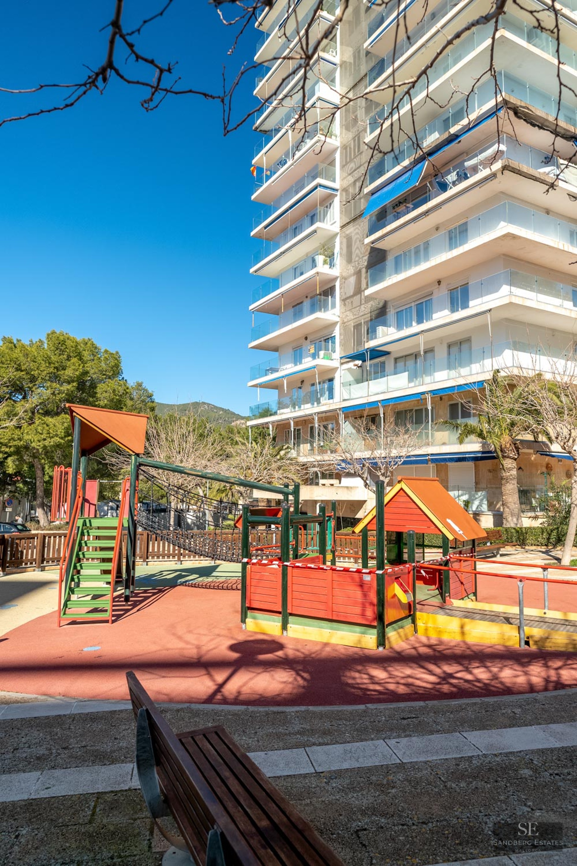 A colorful children's playground with safety flooring in front of a modern high-rise apartment building.