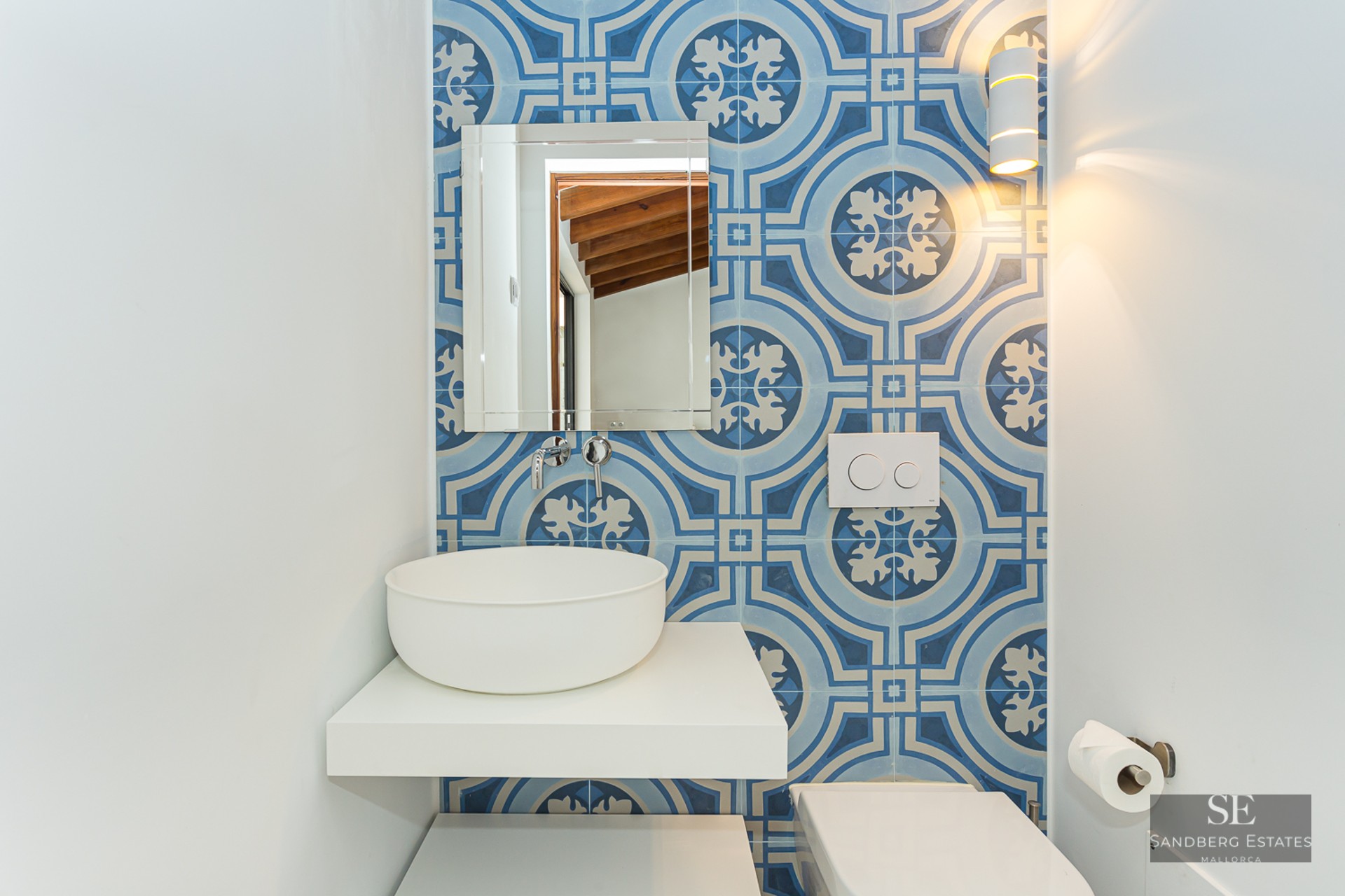 Bathroom featuring blue patterned wall tiles, a white vessel sink on a floating shelf, and a rectangular mirror.