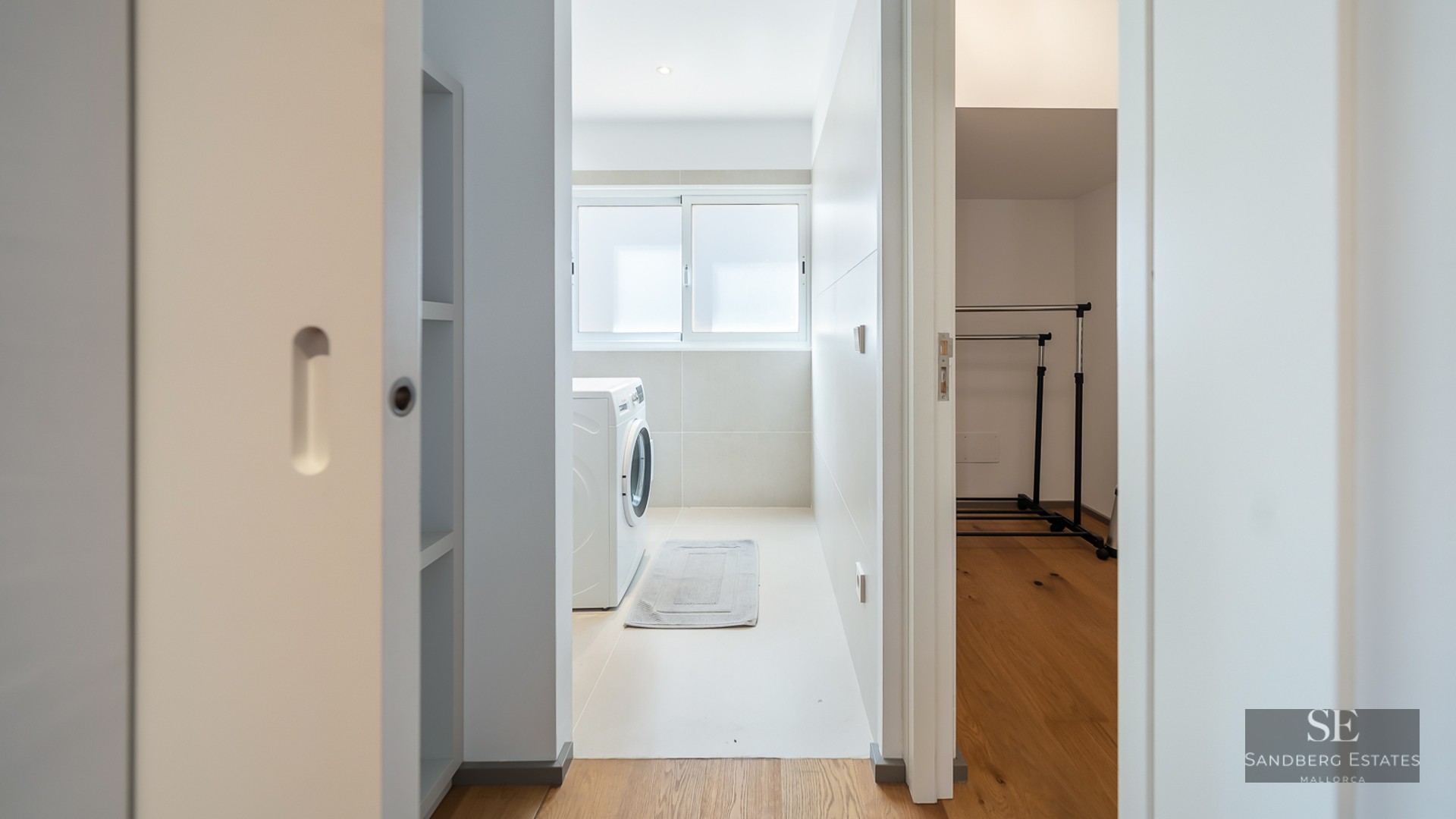 View of a white laundry room with a washing machine and an adjacent walk-in closet with wooden floors.