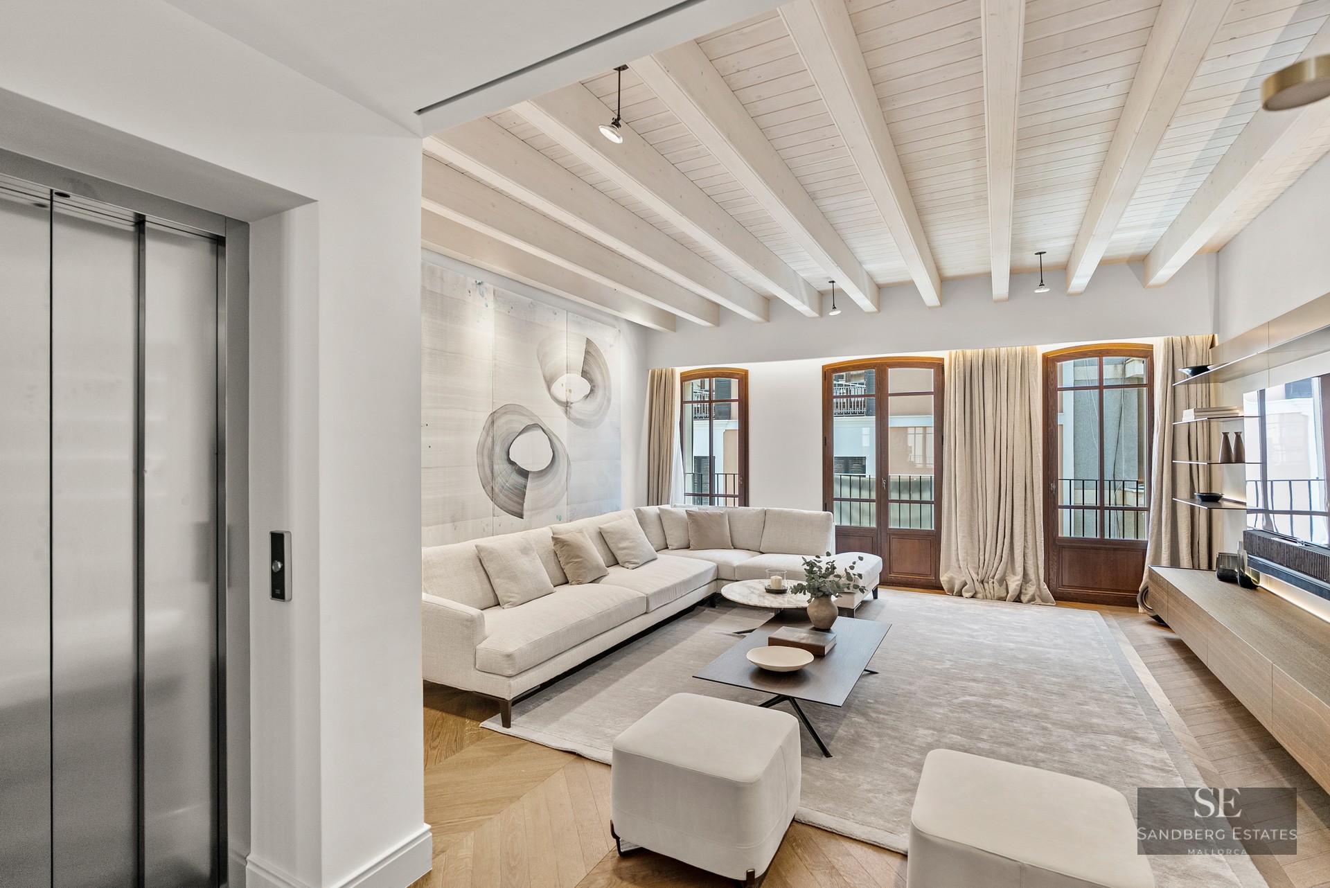 Spacious modern living room featuring a white sectional sofa, wooden ceiling beams, and a private elevator access.